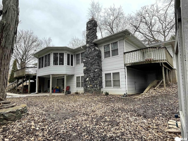 rear view of house with a patio, a chimney, stairway, a sunroom, and a deck