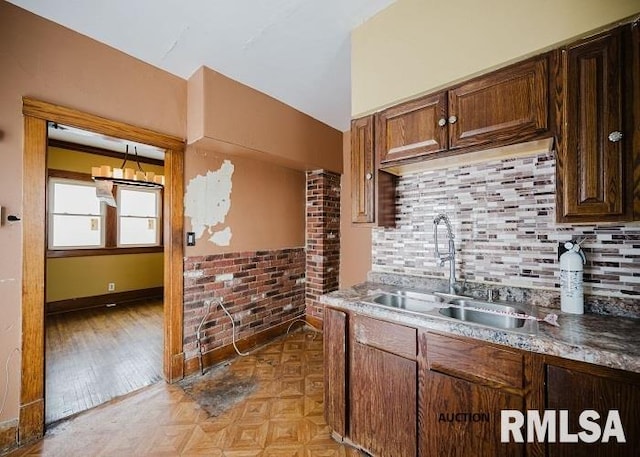 kitchen with parquet floors, decorative backsplash, dark brown cabinetry, a sink, and brick wall