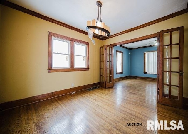 unfurnished room featuring french doors, crown molding, an inviting chandelier, wood finished floors, and baseboards