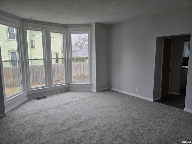 unfurnished room with visible vents, a textured ceiling, baseboards, and carpet flooring