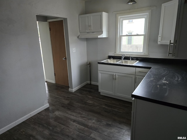 kitchen featuring dark wood-style floors, dark countertops, white cabinets, a sink, and baseboards