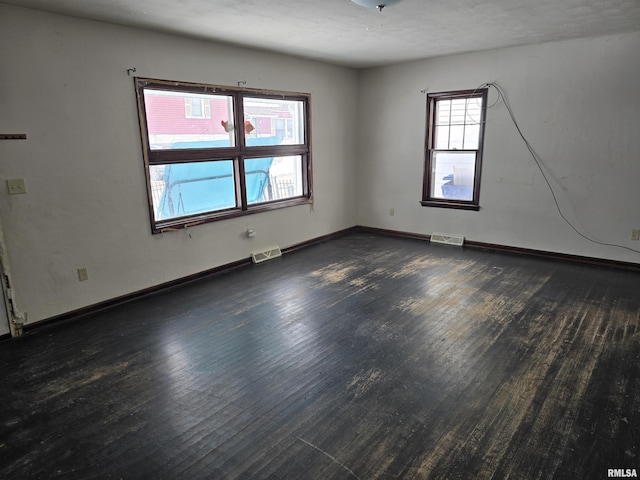 unfurnished room with dark wood-style floors, visible vents, and baseboards