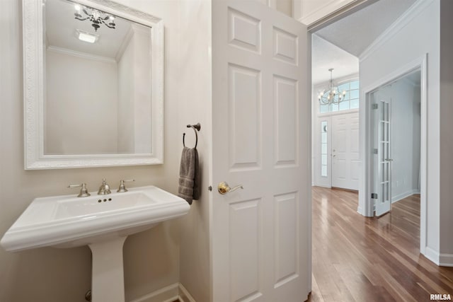 bathroom with a chandelier, crown molding, baseboards, and wood finished floors