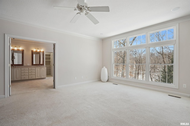 unfurnished bedroom with light colored carpet, visible vents, baseboards, ensuite bath, and crown molding