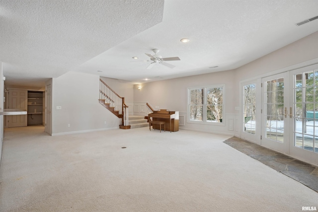 unfurnished living room featuring light carpet, visible vents, stairs, french doors, and a wealth of natural light