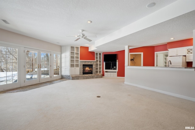 unfurnished living room featuring a fireplace, light colored carpet, visible vents, a textured ceiling, and baseboards