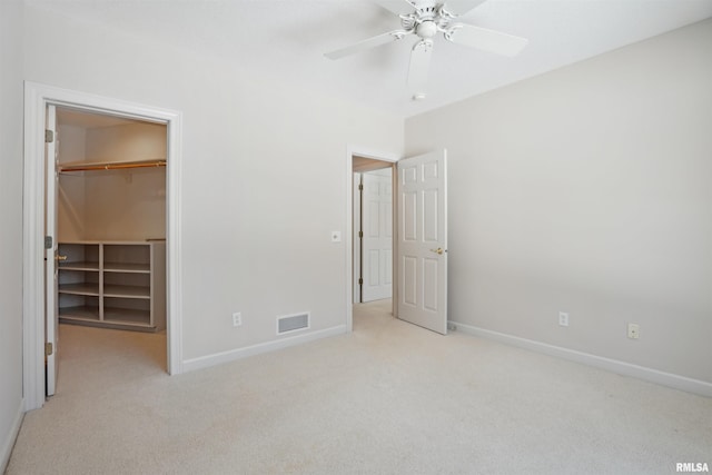 unfurnished bedroom with a walk in closet, a closet, visible vents, light carpet, and baseboards