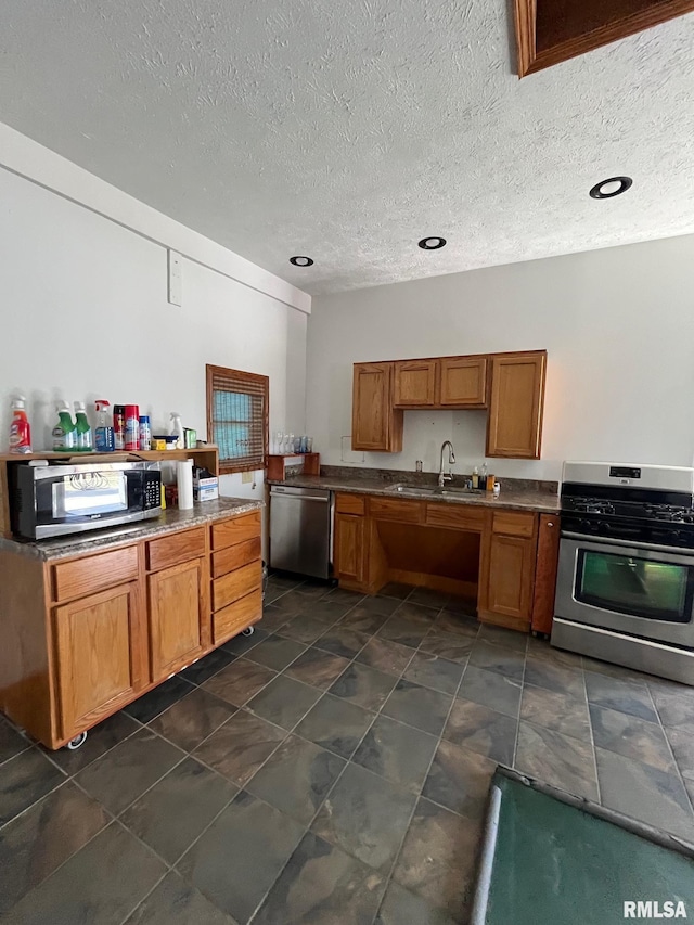 kitchen featuring a textured ceiling, appliances with stainless steel finishes, brown cabinetry, and a sink