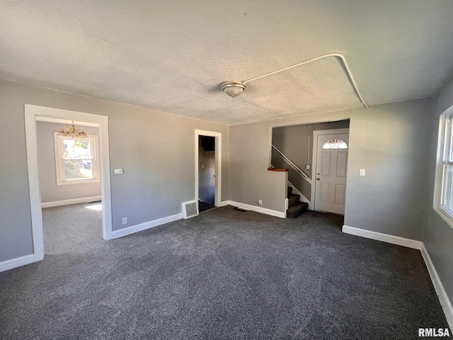 unfurnished living room featuring dark colored carpet, visible vents, a textured ceiling, baseboards, and stairs