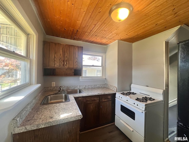 kitchen with wood ceiling, white gas range, light stone counters, and a sink