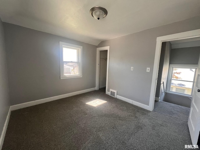 unfurnished bedroom featuring baseboards, multiple windows, visible vents, and dark colored carpet