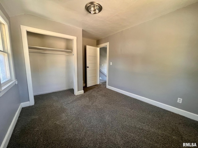 unfurnished bedroom with a closet, dark carpet, and baseboards