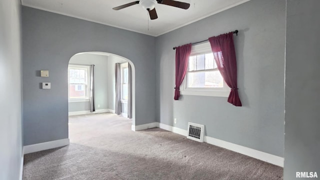 carpeted empty room featuring arched walkways, ceiling fan, visible vents, baseboards, and ornamental molding