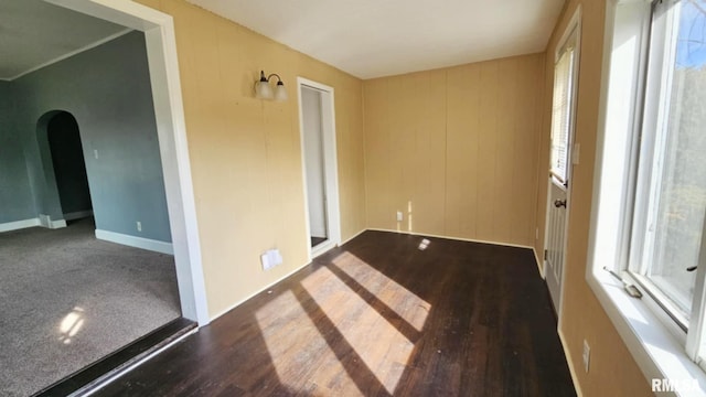 empty room featuring dark wood-style floors, baseboards, and arched walkways