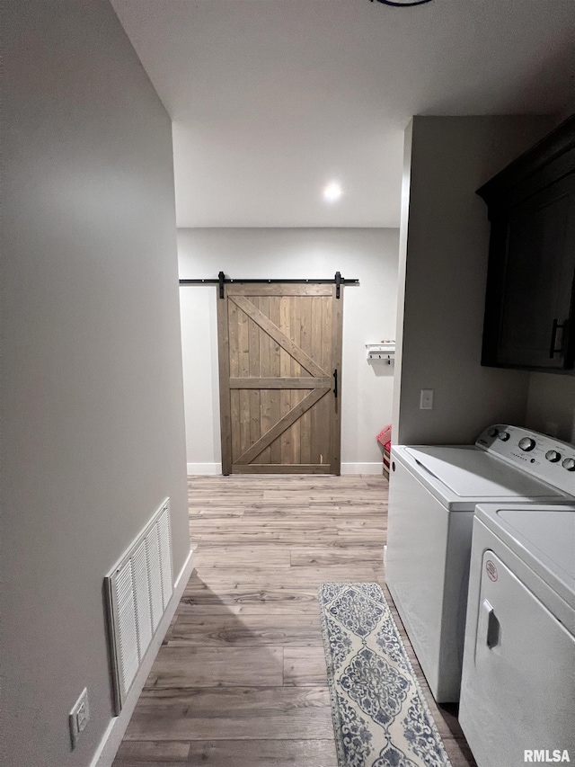 clothes washing area with a barn door, visible vents, light wood-style floors, independent washer and dryer, and cabinet space