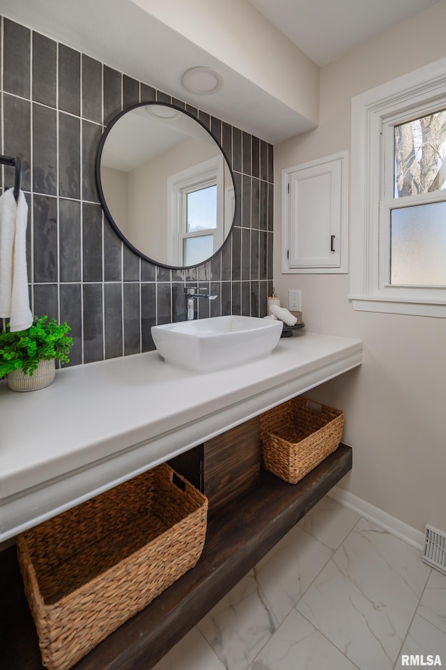 bathroom with visible vents, baseboards, decorative backsplash, marble finish floor, and a sink