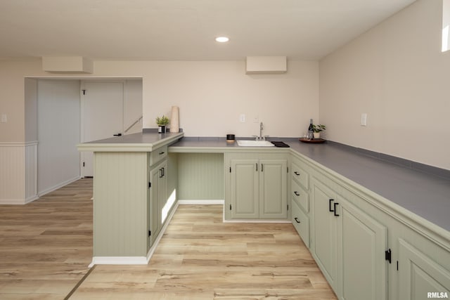 kitchen with green cabinets, a peninsula, a sink, and light wood-style flooring