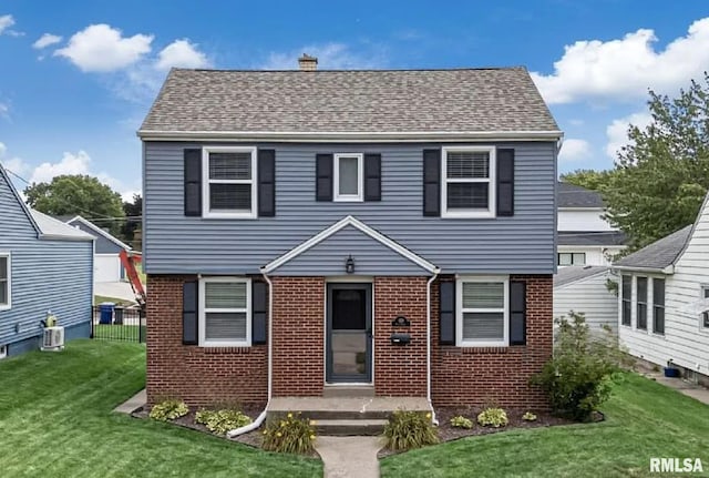 colonial inspired home featuring central AC, brick siding, fence, roof with shingles, and a front lawn