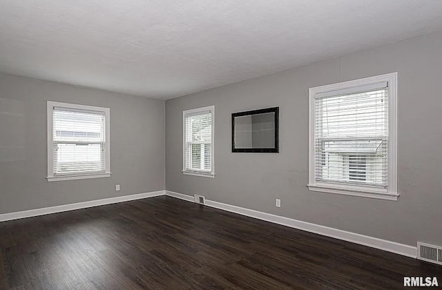 unfurnished room featuring baseboards, visible vents, and dark wood-style flooring