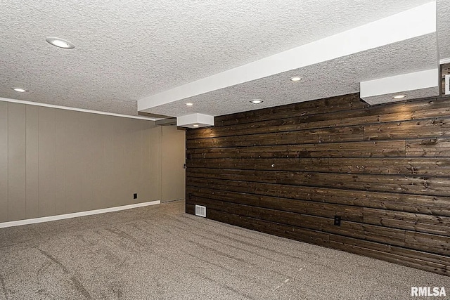 finished below grade area featuring wood walls, carpet, visible vents, and a textured ceiling