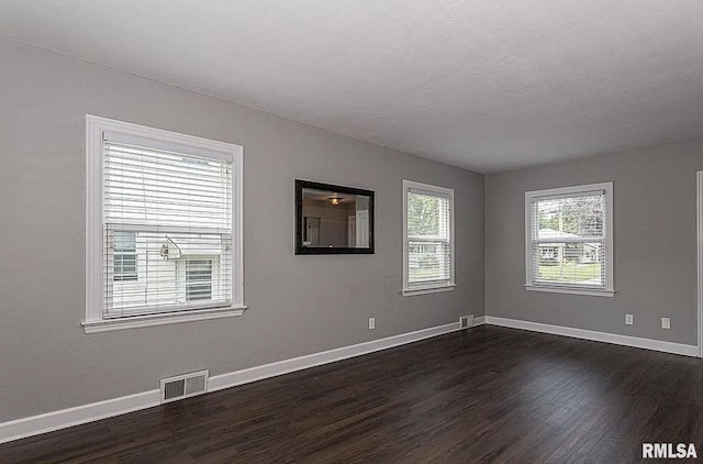 unfurnished room featuring dark wood-type flooring, visible vents, and baseboards