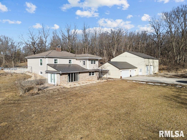 rear view of property featuring an outbuilding, a yard, a detached garage, and a chimney