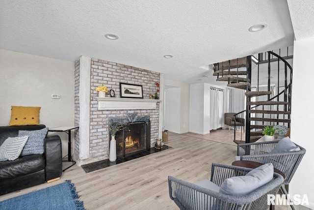 living room featuring stairs, a brick fireplace, wood finished floors, and a textured ceiling