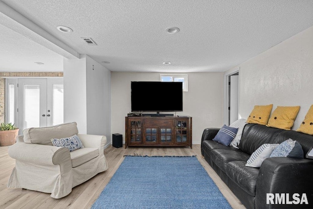 living area with baseboards, visible vents, light wood-style flooring, french doors, and a textured ceiling