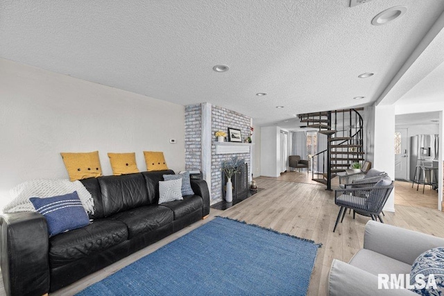 living area with stairway, a fireplace, a textured ceiling, and wood finished floors