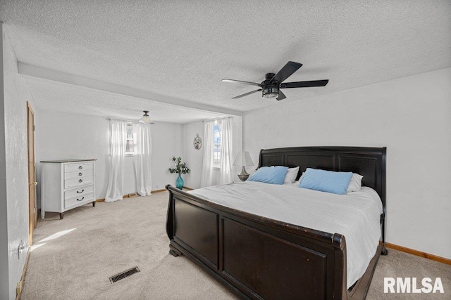 bedroom with visible vents, light colored carpet, a textured ceiling, and a ceiling fan