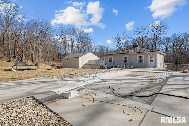 rear view of property featuring a trampoline, a tile roof, a chimney, an outbuilding, and a patio