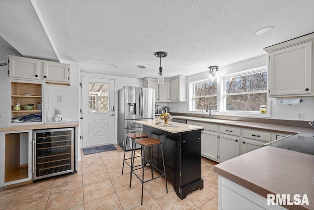 kitchen with pendant lighting, beverage cooler, a kitchen island, a textured ceiling, and stainless steel fridge