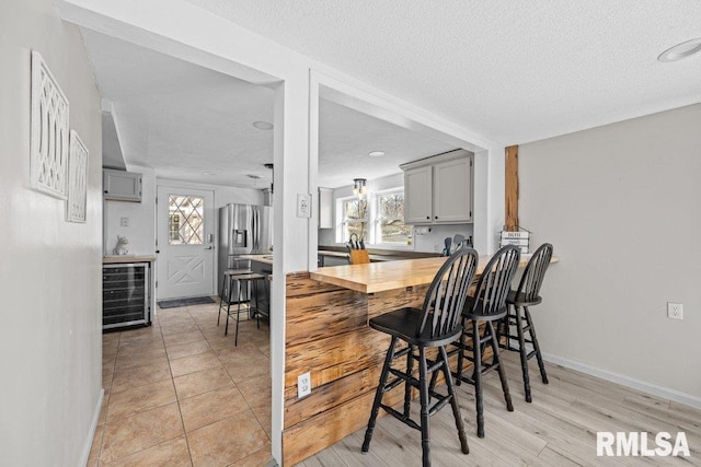 kitchen featuring beverage cooler, gray cabinetry, baseboards, and stainless steel refrigerator with ice dispenser