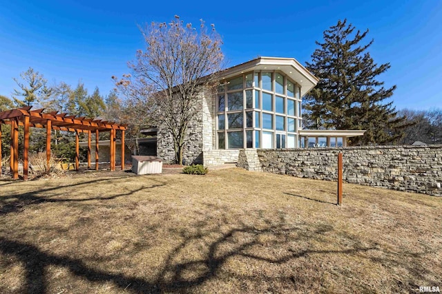 back of house with stone siding, a lawn, and a pergola