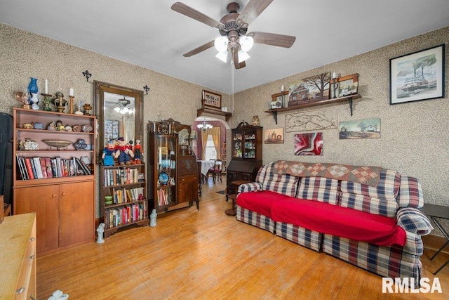 living area featuring ceiling fan with notable chandelier, wallpapered walls, and wood finished floors