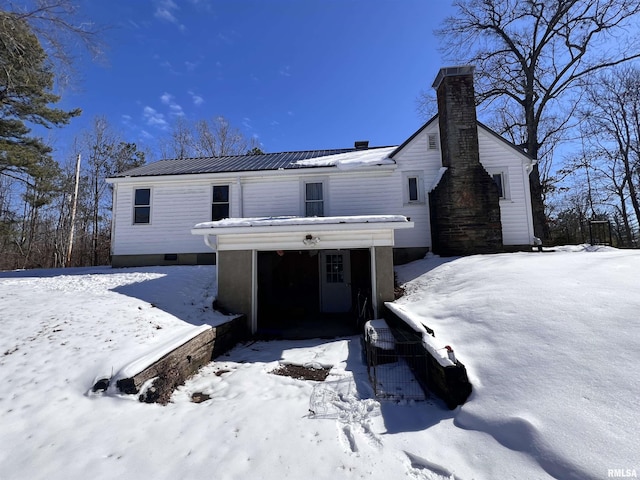 snow covered house featuring a garage, metal roof, and a chimney