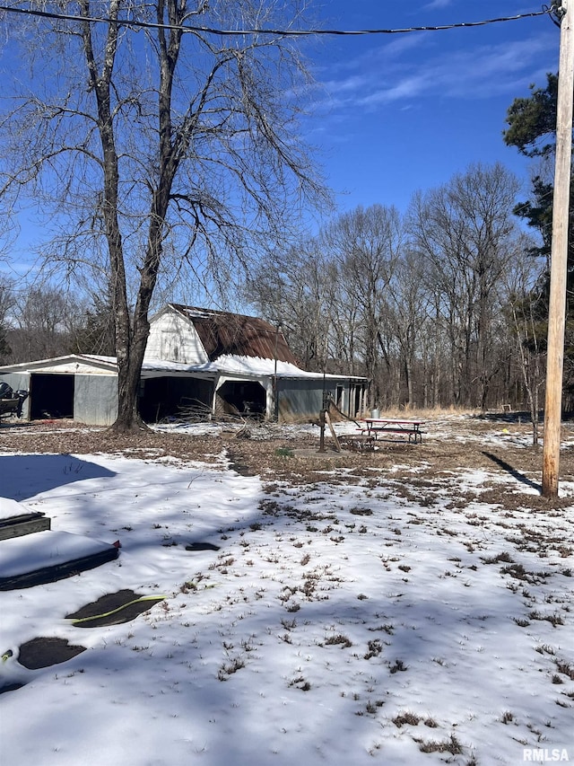 snowy yard featuring a barn, a detached garage, and an outdoor structure