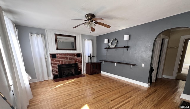 unfurnished living room featuring arched walkways, wood-type flooring, baseboards, and a brick fireplace