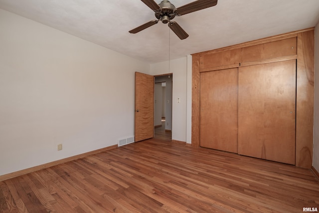 unfurnished bedroom with wood finished floors, a ceiling fan, visible vents, baseboards, and a closet