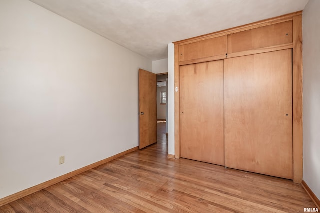 unfurnished bedroom featuring a closet, baseboards, and light wood finished floors