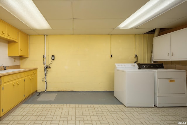 clothes washing area with concrete block wall, cabinet space, a sink, and washer and clothes dryer