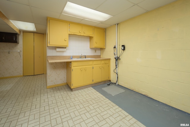 kitchen with concrete block wall, a paneled ceiling, light countertops, a sink, and baseboards