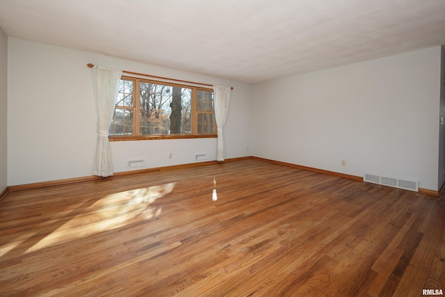 unfurnished room with wood finished floors, visible vents, and baseboards