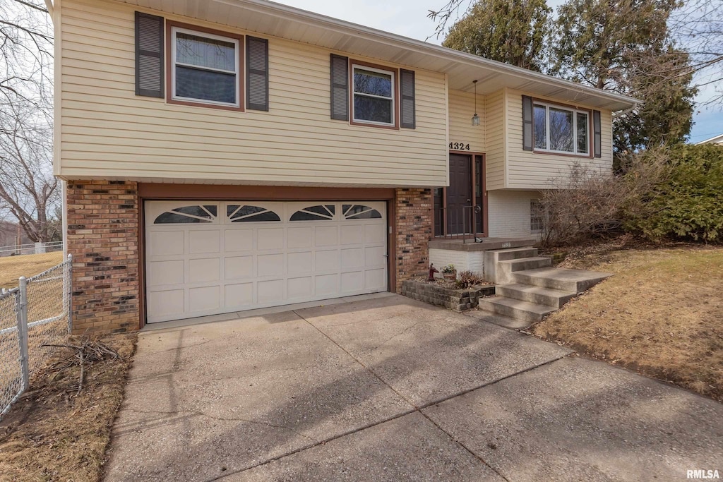 bi-level home with brick siding, fence, driveway, and an attached garage