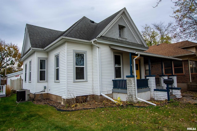 view of front facade featuring cooling unit, covered porch, roof with shingles, and a front yard