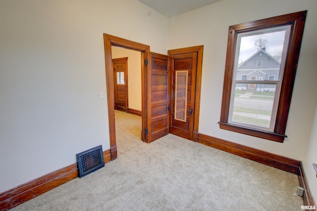 empty room featuring light colored carpet, visible vents, and baseboards