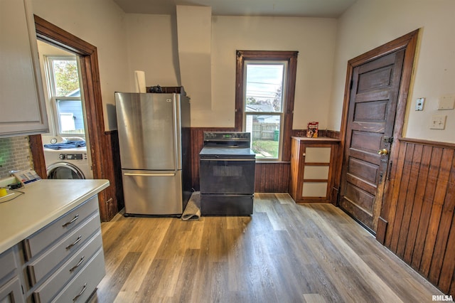 kitchen featuring washer / dryer, a wainscoted wall, freestanding refrigerator, black / electric stove, and light countertops