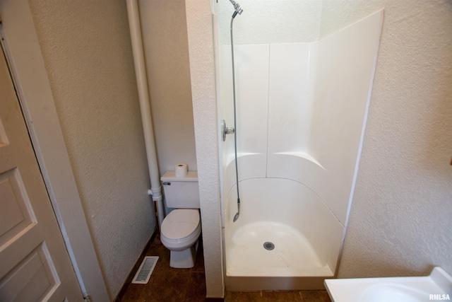 bathroom with toilet, a textured wall, a stall shower, and visible vents