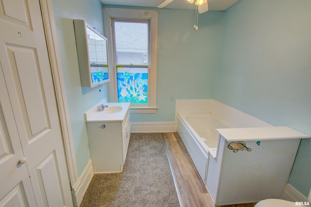 full bath with a garden tub, a ceiling fan, vanity, wood finished floors, and baseboards