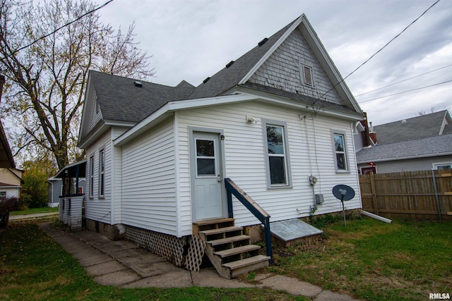 rear view of property with entry steps, a shingled roof, a lawn, and fence